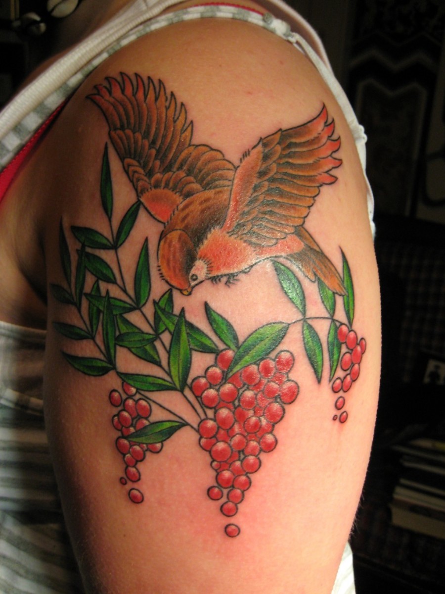 En levende tatovering av en fugl som svever over røde bær.