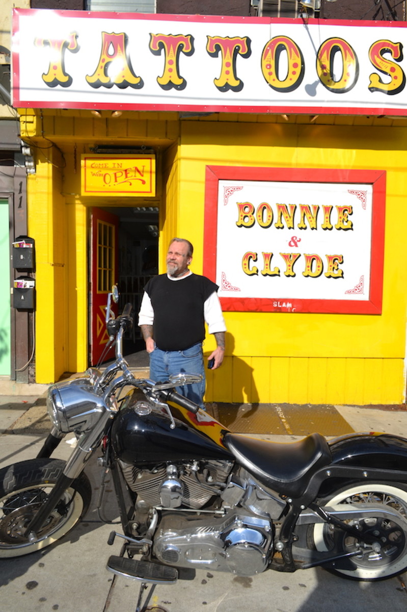 Sailor Eddie se svou motorkou před svým obchodem, Bonnie & amp; Clydeův tetovací salon.