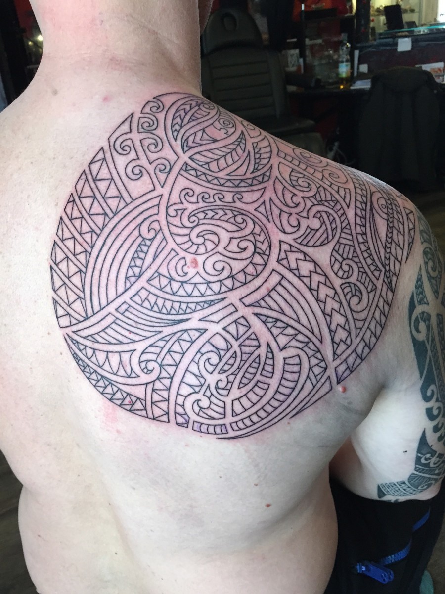 Maorské tetování zakrývající mužské rameno, čepici a čepel.