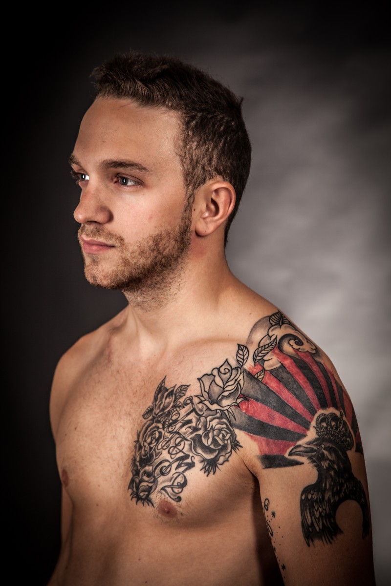 Muž s tetováním, které mu zakrývalo hrudník, čepici na rameni a paži.