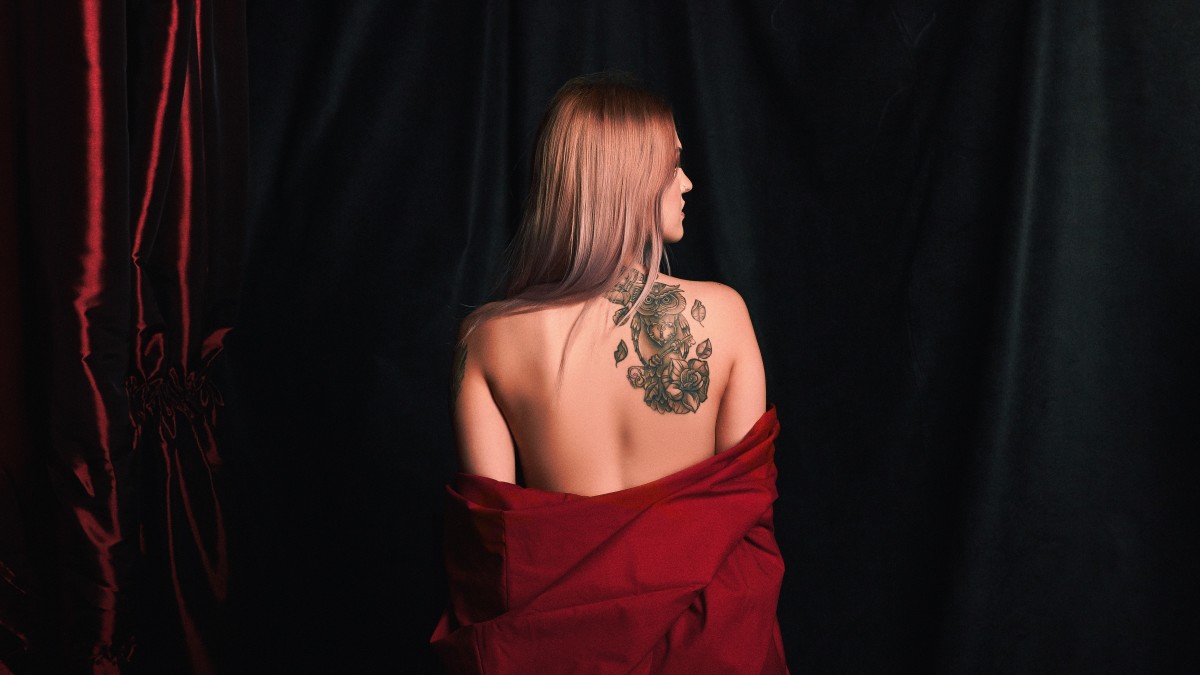 Kvinne med stor skulder -tatovering av en ugle og blomster.